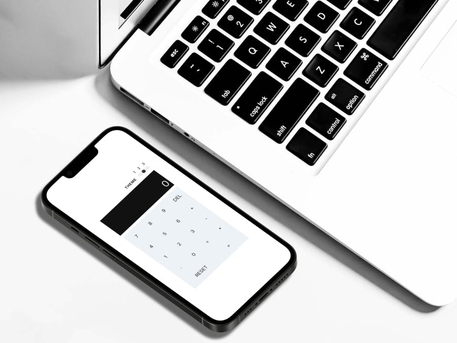 A white-themed calculator application on an iPhone screen, resting next to a laptop
