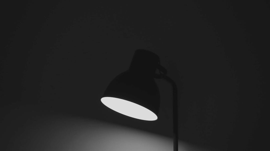 A black desk lamp, on and facing the surface