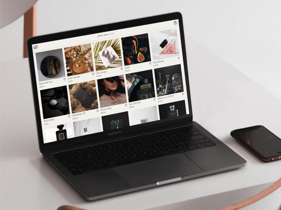 A luxury shopping site on a Macbook, resting on a white table with a mobile next to it