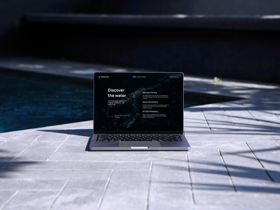 A MacBook in front of a pool showing a website